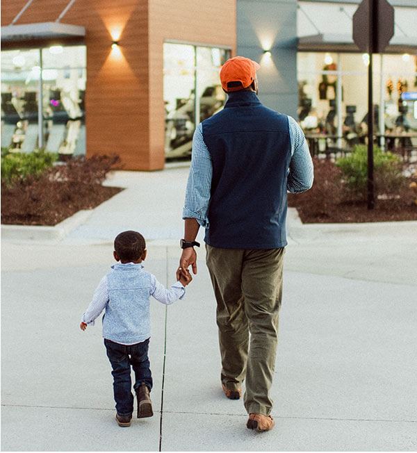 Father holding son's hand at outdoor retail area.