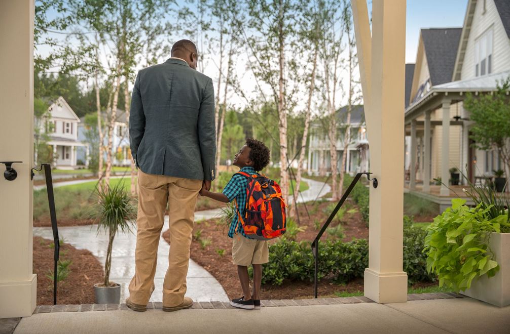 A father and son hold hands on a porch about to go to school