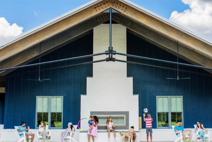 Group of people sitting and playing in front of a modern blue and white house with a tall peaked roof in Summerville.